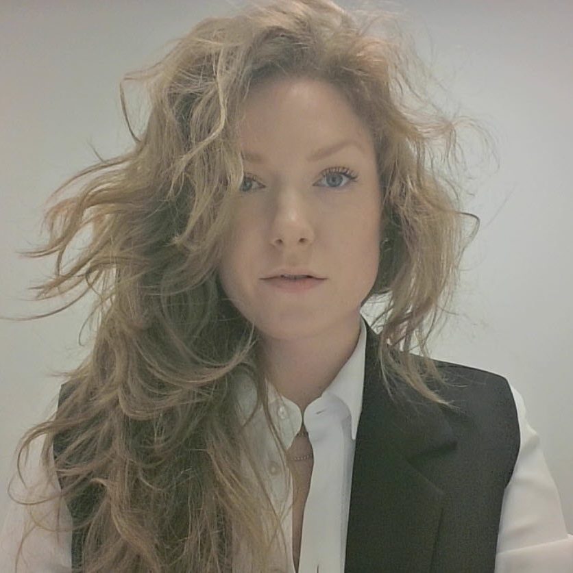 Julia Rhault in a white blouse and black vest with tousled natural wavy hair.